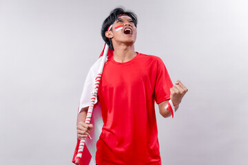 A young man celebrates Indonesia’s Independence Day with enthusiasm, wearing red and white, holding the Indonesian flag, and expressing national pride in a victory pose with a loud cheer.