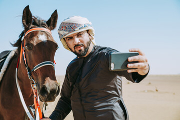 Young adult with Kandura, the emirates traditional clothes, riding his horse in the desert