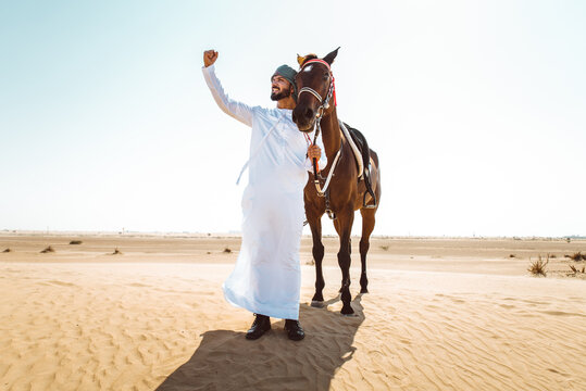 Young adult with Kandura, the emirates traditional clothes, riding his horse in the desert