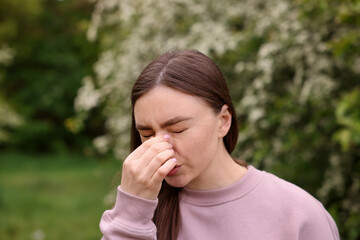 Woman suffering from seasonal pollen allergy near blossoming shrub on spring day, space for text