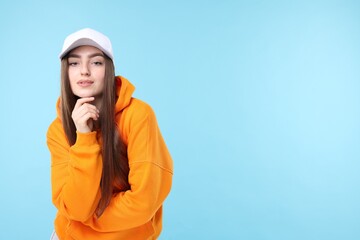 Portrait of beautiful woman in stylish baseball hat on light blue background. Space for text