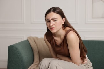 Woman suffering from abdominal pain on sofa at home