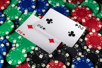 Obraz premium Colorful poker chips are scattered around two playing cards showing the number two, suggesting an engaging and competitive card game taking place among friends