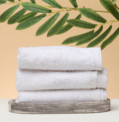 A stack of white folded towels lies on a marble stand, beige background