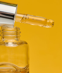 A clear glass dropper bottle with a silver cap and a white dropper dripping amber liquid