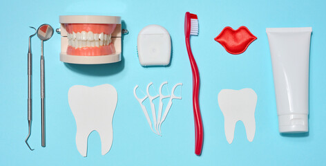 Set of oral hygiene products and tools, tube of toothpaste, toothbrush, dental floss, dental instruments, and jaw model on blue background.