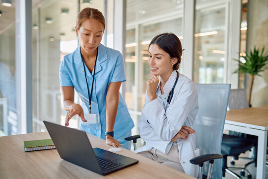 Nurse collaborating with medical doctor while presenting information on a laptop in a bright hospital office, enhancing teamwork and communication