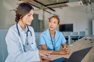 Two female doctors engaging in a discussion about a diagnosis while using a laptop in a hospital...