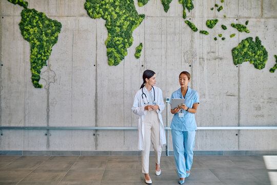 Doctor and nurse walking in hospital corridor with a world map made of moss discussing about global health
