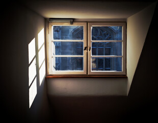 Window in a dark room letting in bright daylight. The contrast between light and shadow is strong.