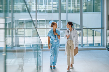 Doctor and nurse walking and discussing a medical case in a modern, bright hospital corridor, showcasing teamwork and collaboration in healthcare