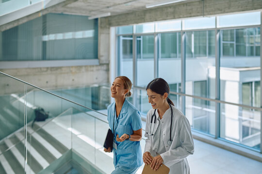 Two female doctors are walking down the hospital corridor, smiling and talking about their daily duties