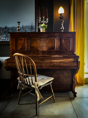 An old piano with wooden chair in a room with yellow curtain. The scene feels nostalgic and...