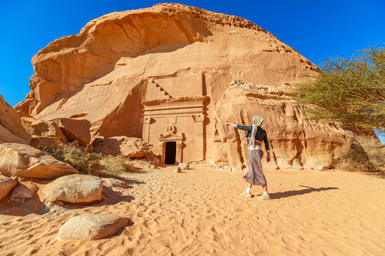 Tourist is pointing at a nabataean tomb carved into the Jabal AlBanat sandstone rock face in the Hegra Archaeological Site Madain Saleh, located in Al-Ula, Saudi Arabia, a UNESCO World Heritage site