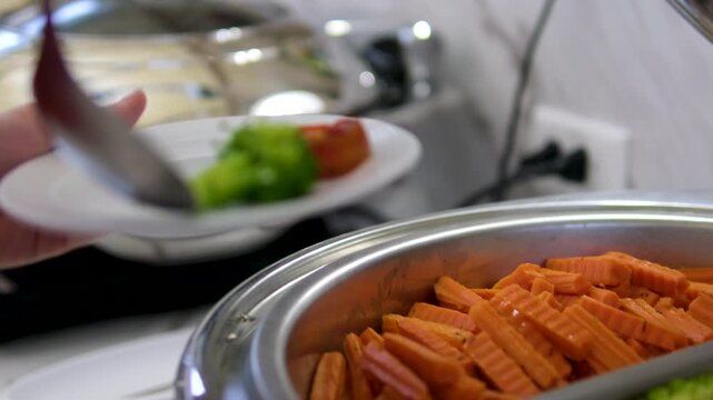 carrots in the buffet Fresh Vegetables in Serving Bowl with Silver Spoon including Tenderstem Broccoli, Carrots, Cauliflower, Baby Corn. Healthy Food in Natural Light.