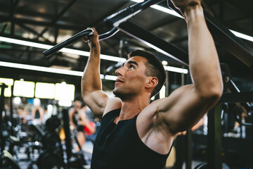 young man athlete doing shoulder workout on the gym machine