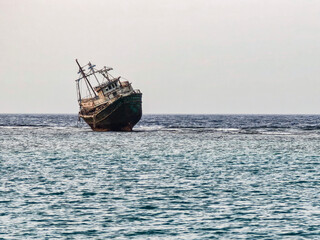 An old ship rests in clear water, slightly tilted – abandoned calm in daylight.