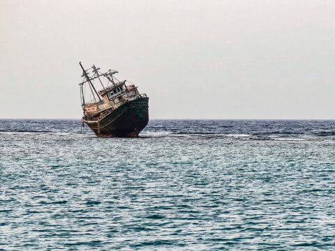 An old ship rests in clear water, slightly tilted – abandoned calm in daylight. - Powered by Adobe