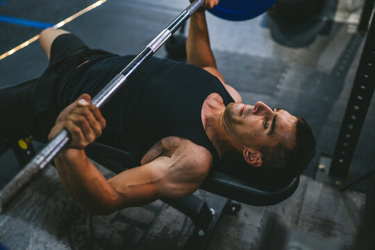 Handsome young athlete man doing bench press workout in gym