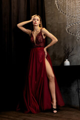 Stylish model poses elegantly in a deep red evening gown with thigh-high slit, showcasing fashion...