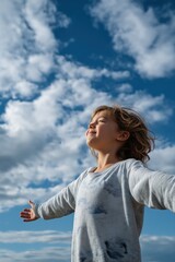 Joyful caucasian child with open arms embracing the sky under cloudy blue sky