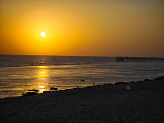 The sun sets over the sea, a pier at the right edge – peaceful evening moment.