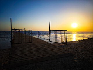 Fototapeta premium An open gate leads to the sea in the setting sun – a symbol of freedom and openness.