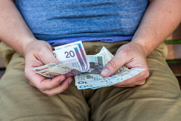 Man Holding Polish Zloty Banknotes in Wallet – Personal Finance Concept. Close-up of a man sitting on a bench and holding a black leather wallet with visible Polish zloty banknotes.