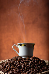Coffee, beautiful cup of coffee on a heap of coffee beans in a straw sieve, abstract background, selective focus.