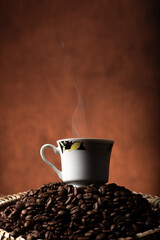 Coffee, beautiful cup of coffee on a heap of coffee beans in a straw sieve, abstract background, selective focus.