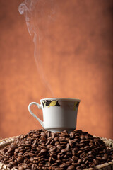 Coffee, beautiful cup of coffee on a heap of coffee beans in a straw sieve, abstract background, selective focus.