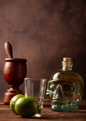 Cachaça from Brazil, bottle of cachaça from Brazil in the shape of a skull, lemon accessories on rustic wood and abstract background, low key photo, selective focus.
