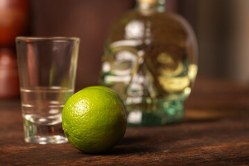Cachaça from Brazil, bottle of cachaça from Brazil in the shape of a skull, lemon accessories on rustic wood and abstract background, low key photo, selective focus.