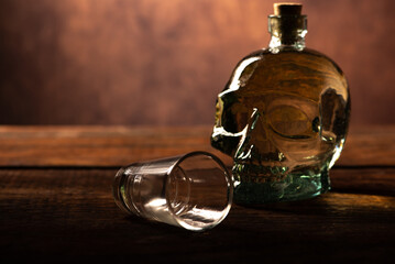 Cachaça, Brazilian cachaça bottle in the shape of a skull and a glass, on rustic wood and abstract background, low key photo, selective focus.