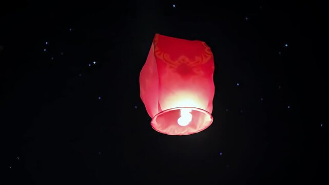 Glowing red lantern floats upward into the dark starry sky