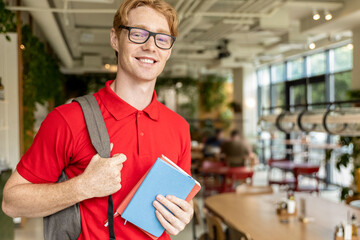 Young ginger man in eyeglasses looking confident and smiling nicely
