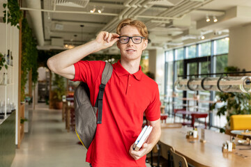 Smiling young guy with books in hands looking positive and joyful