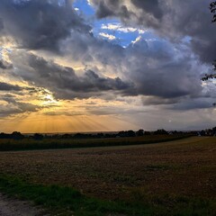 Dramatic landscape with sun rays through clouds over farmland