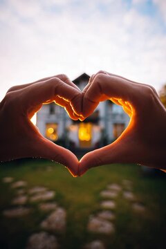 a home owner makes a heart shape with her hands in front of a beautiful home exterior, golden hour light - love my home, remodel, purchase, paint or construction - real estate agent, friendly concept