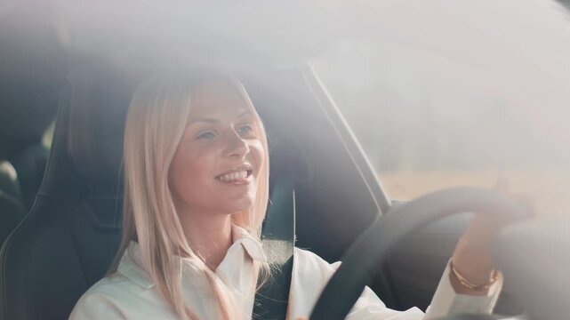 Positive blonde female holding steering wheel with both hands while smiling softly. Driving calmly and appreciating surroundings. Enjoying peaceful ride and staying relaxed during clear day.