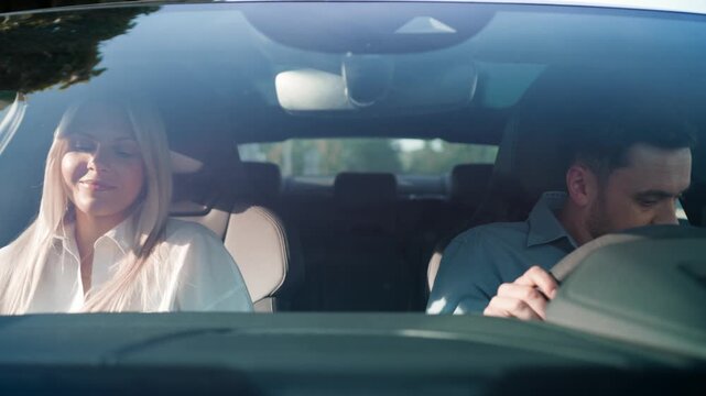 Caucasian man and woman sitting in front seats of parked car with upper bodies slightly turned away. Both wearing formal shirts and staying silent. Waiting or pausing conversation during quiet moment.