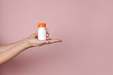 Elegant hand holding blank bottle mockup on pink background. Package for cosmetics product, nutritional supplements, vitamins, spa, beauty and luxury. Space for text