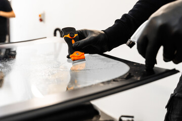Technician uses scraper to clean the surface of a new windshield post-replacement. Technician...