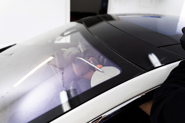 Auto technician separates windshield using fine wire and scraping blade. Car windshield replacement process. Windshield removal in progress using specialized cutting wire and scraper tool.