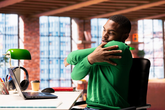 Remote employee in home office stretching joints after sitting at desk too long. Freelancer in living room doing muscle exercises after feeling pain from incorrect posture