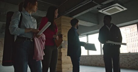 A multinational business team discusses construction plans in a new office space. The diverse group collaborates, pointing and reviewing blueprints. - Powered by Adobe