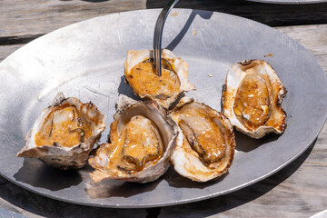 Close-up of grilled oysters with golden orange roe on a large round silver platter at a rustic table