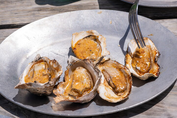 Grilled oysters served open-faced on a metal platter with utensils, revealing golden-orange filling inside the shell