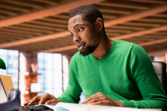Man at home office desk crosschecking information between laptop screen and paper files, seeing inaccuracies. Remote worker confused by missing data in documents, comparing with notebook display