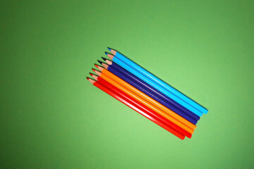 Diagonal arrangement of sharpened red, orange, blue, and purple color pencils on vibrant green...